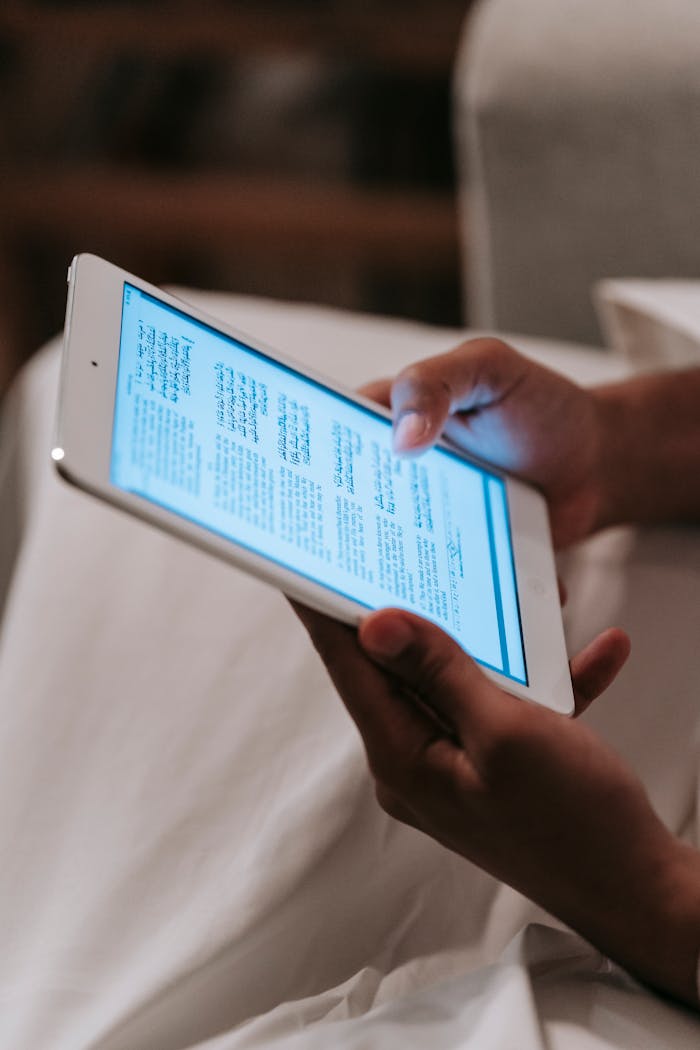 A person reading text on a digital tablet screen indoors, focusing on technology and modern reading habits.